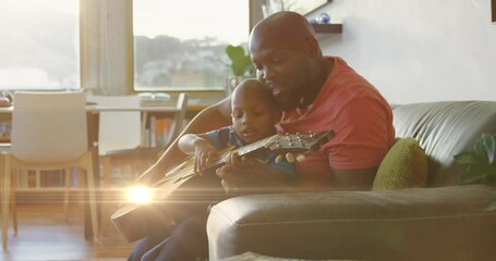 Wall Mural - Animation of light spots over happy african american father playing guitar with son