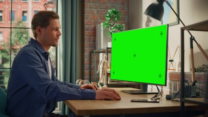 Poster - Young Handsome Man Working from Home on Desktop Computer with Green Screen Mock Up Display. Male Checking Corporate Accounts, Messaging Colleagues. Loft Living Room with Big Window. Zoom In Shot.