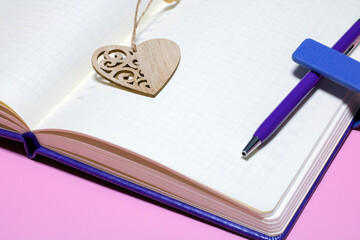 Open blank notebook in a cage with a bookmark in the shape of a heart on a pink background.