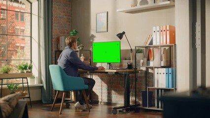 Poster - Young Handsome Man Working from Home on Desktop Computer with Green Screen Mock Up Display. Creative Male Checking Social Media, Browsing Internet. Living Room in Bright Loft Apartment. Wide Shot.