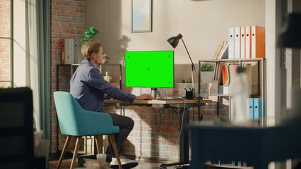 Aufkleber - Young Handsome Man Working from Home on Desktop Computer with Green Screen Mock Up Display. Male Checking Corporate Accounts, Messaging Colleagues. Loft Living Room with Big Window.  Wide Shot.
