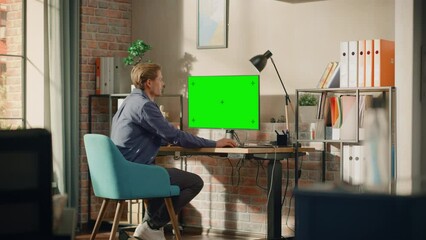 Poster - Young Handsome Man Working from Home on Desktop Computer with Green Screen Mock Up Display. Male Checking Corporate Accounts, Messaging Colleagues. Loft Living Room with Big Window. Zoom In Shot.