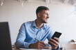 © BullRun - Cheerful male student with modern smartphone device smiling during time for studying indoors, happy freelancer with digital cellphone and laptop technology enjoying remote job in coworking space