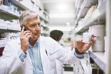 Poster - We need more pain killers. Shot of a focused mature male pharmacist talking on his cellphone while reading the back of a medication box.