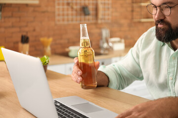 Wall Mural - Man with laptop drinking beer in kitchen