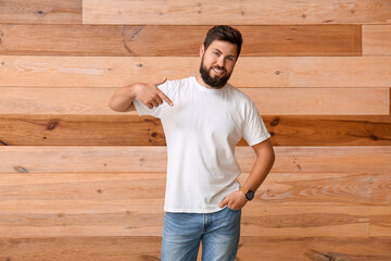 Wall Mural - Handsome man pointing at white t-shirt on wooden background