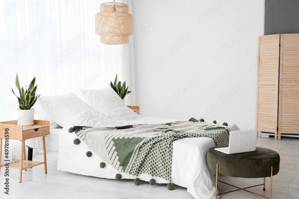 Comfortable bed, houseplants and laptop in room