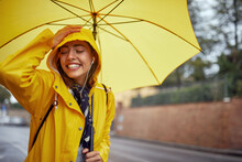 Close-up Of A Young Cheerful Woman With A Yellow Raincoat And Umbrella Who Is In A Good Mood While Walking The City On A Rainy Day And Posing For A Photo. Walk, Rain, City