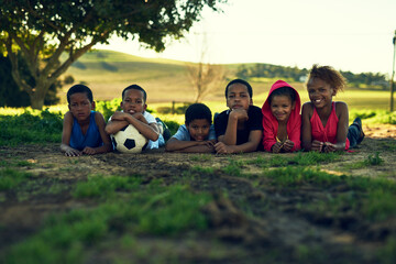 Getting some fresh air and exercise. Shot of a group of children lying together with a soccer ball on some grass outside.