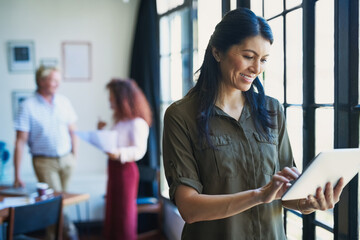 Poster - Management in the age of the app. Shot of a mature woman using a digital tablet with her team in the background of a modern office.