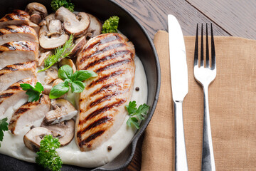 Wall Mural - Roasted chicken fillet and mushrooms with herb in the frying pan on the wooden table close-up.