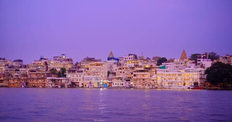Fototapete - Famous luxury Udaipur City Palace, Lal ghat, houses on bank Pichola lake illuminated on sunset with water ripples - Rajput architecture of Mewars. Udaipur, Rajasthan, India. Horizontal pan
