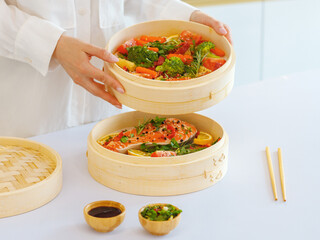 a girl in white clothes cooks steamed food in a bamboo steamer. morning mood, the concept of healthy eating