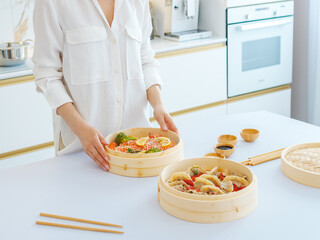 a girl in white clothes cooks steamed food in a bamboo steamer. morning mood, the concept of healthy eating