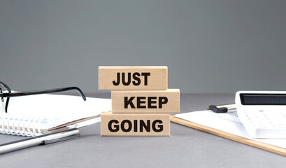JUST KEEP GOING text on wooden block with notebook,chart and calculator, grey background