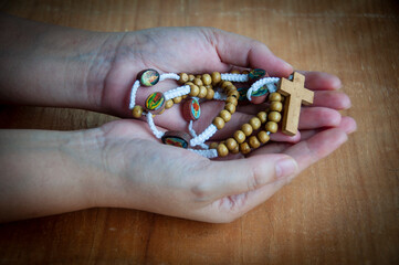 Wall Mural - Hand holding Holy Rosary with wooden table background. Religious concept