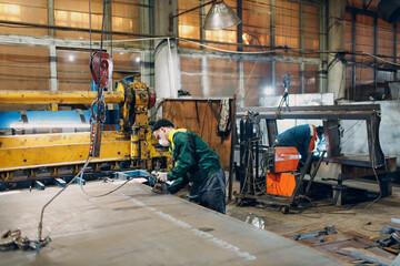 Wall Mural - Worker man lift metal sheet with crane chain hoist with remote controller and hook at industrial factory plant