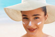 Beautiful Young woman with sun cream on face. Female in hat applying  moisturizing lotion on skin.Skin care. Sun protection. Suntan