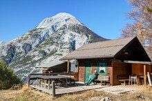A Mountain Hiker Enjoys The Midday Sun On A Lonely, Dilapidated Mountain Hut Against The Impressive Backdrop Of The Mount Hohe Munde In The Tyrolean Alps.