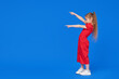 Full length portrait of a  little toddler girl child standing isolated over blue background. Points hands to the left side. Advertising childrens product