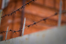 Prison Fence With Sharp Spikes And Barbed Wire Close-up. Rusty Barbed Wire On Metal Gates.