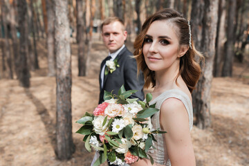 Wedding couple in the park. An elegant bride of European appearance and a groom in a black suit.