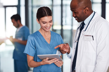 You have an appointment at three oclock today. Shot of two cheerful young doctors having a discussion over a digital tablet inside of a hospital.