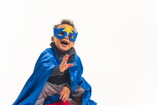 Studio Shot Of A Little Biracial Boy Toddler In A Hero Costume With A Dark Blue Mask With A Star And A Cape Laughing Out Loud Over White Background. High Quality Photo