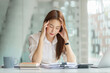 © amnaj - Overworked and stressed young Asian woman sitting at workplace in office.