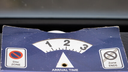 Close up of a blue parking disk beside a windshield indicating arrival time