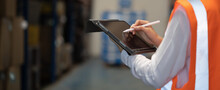 Panoramic Close Up Hand Of Smart Engineer Man Warehouse Management System.Worker Hands Holding Tablet With Pen On Blurred Warehouse As Background. Logistic, Import Export Concept.