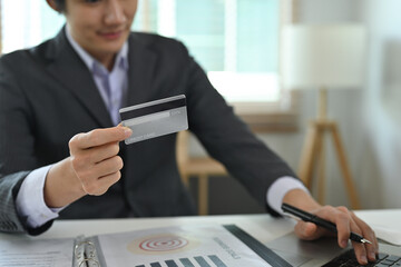 Poster - Close up with Businessman's working on a laptop and holding a credit card while sitting at the office desk, for finance, business and technology concept.
