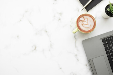 Wall Mural - White marble office desk table with laptop computer, cup of latte coffee and office supplies. Top view with copy space, flat lay.