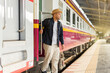 © Patcharanan - Young asian man traveler backpack in the train station. Backpacker male wear hat and denim jacket at the railway are going down the train ladder. Travel concept. The concept of a man traveling alone.
