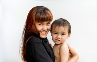 Wall Mural - Happy mother with her baby on isolated white background. Mom wearing black shirt holding her son and smiling merrily. Young attractive happy mother smiling hugging looking at her littel baby.