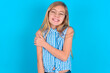 People, lifestyle, youth and happiness concept. Shy pretty little kid girl with glasses wearing plaid shirt over blue background , feeling happy hugging herself.
