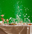 fragments of dishes and bread flying over the table during an explosion on a green background