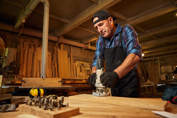 Wall Mural - Senior Professional carpenter in uniform working of manual milling machine in the carpentry workshop