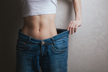 Closeup Cropped View Of Skinny Woman Showing Flat Stomach Pulling Oversized Big Blue Pants Jeans