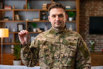Indoor shot of military man wearing camouflage uniform and hat holding house keys, mortgage assistance from a veterans organization, extremely happy soldier male.