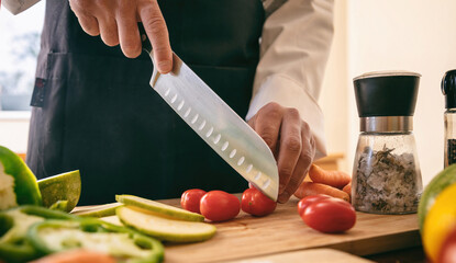 Chef cut tomato with a knife on a chopping board, close up. Fresh vegetable on kitchen table.