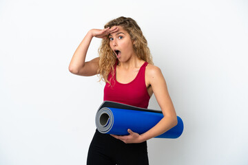 Wall Mural - Young sport blonde woman going to yoga classes while holding a mat isolated on white background doing surprise gesture while looking to the side