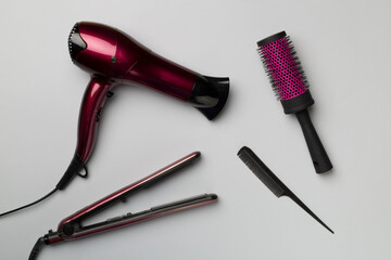 Hair dryer, straightener and brush on color background, top view