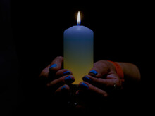 Płonąca świeca Trzymana W Kobiecych Dłoniach. Świeca Ma Odcień Niebieski I żółty. Na Takie Same Kolory Pomalowane Są Paznokcie. Jest To Symbol Solidarności Z Ofiarami Wojny W Ukrainie,