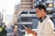 © Meeko Media - A trendy Asian businessman stands on city balcony with tablet and headphones