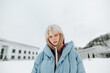 © bodnarphoto - Portrait of a young girl with blond hair and in warm casual clothes stands on a snowy street and looks at the camera.
