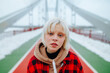 © bodnarphoto - A close-up portrait of a girl in a blonde-haired shirt standing on a snow-covered bridge in winter and posing for the camera with a serious face.