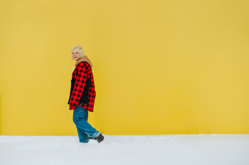 Wall Mural - Smiling girl in casual clothes walks in the winter snow on a background of yellow wall and looks at the camera with a smile on his face.