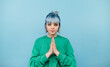 © bodnarphoto - Beautiful hipster girl with blue hair in a green sweater stands on a blue background and prays with a serious face.