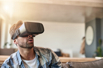 Poster - Dont just watch a movie, experience it. Shot of a young man using a virtual reality headset on the sofa at home.